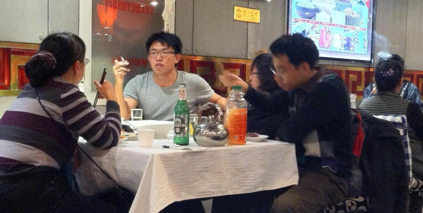 Smokers at tables flanking a no smoking sign in a Beijing restaurant.